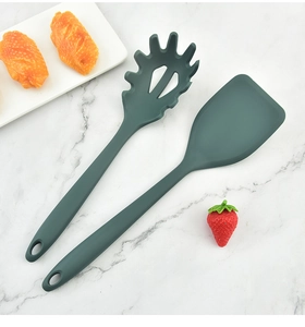 Close-up of deep green heat-resistant silicone spatula and pasta server set on marble