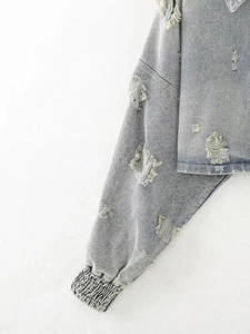 Detail shot of grey denim jacket showing distressed ripped texture and elastic cuffs