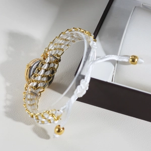 Detail of women's gold quartz watch with white braided strap on a jewelry box
