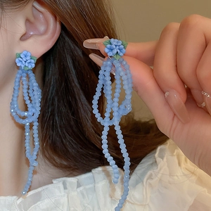 Détail de boucles d'oreilles fleur bleue à pampilles portées par un mannequin
