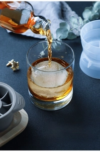Macro view of whiskey pouring over a large clear ice ball made with a silicone mold