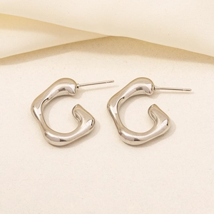 Detail of silver G-shaped 304 stainless steel earrings on a soft beige fabric background