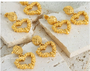 Macro detail of gold-plated heart earrings with woven texture on stone background
