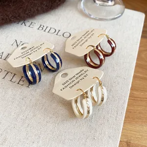 Three pairs of vintage C-shaped gold hoop earrings in blue, brown, and cream enamel finish