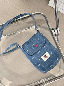 Süße blaue Denim-Umhängetasche mit Schleifenstickerei und Katzen-Aufnäher auf einem Stuhl