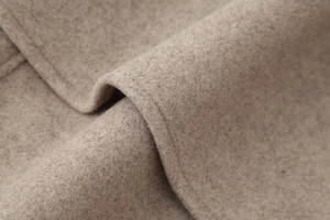 Macro shot of beige wool jacket fabric showing soft texture and premium stitching detail