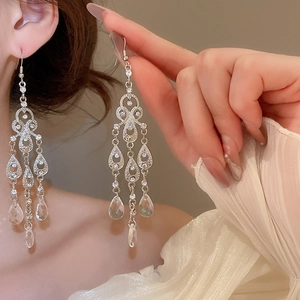 Detail of silver drop earrings with crystals held by model on warm beige background