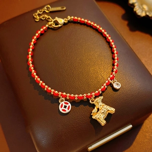 Close-up of woven red cord bracelet with gold pony pendant and coin charm on leather box