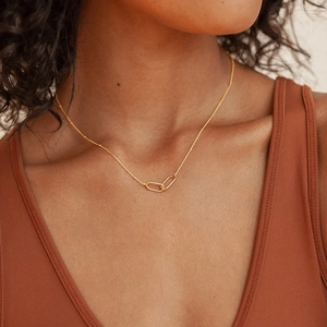 Minimalist gold-tone interlocking oval pendant necklace worn on a female model