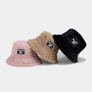 Three plush winter bucket hats in pink, beige, and black with camera heart patches