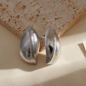 Minimalist silver geometric leaf earrings with brushed texture on a stone background