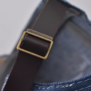 Detailed view of bronze metal buckle and brown leather strap on denim baseball cap