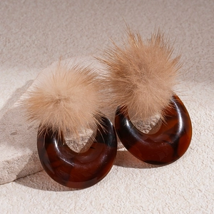 Retro resin hoop earrings with fluffy brown pom pom and silver needles on a textured stone
