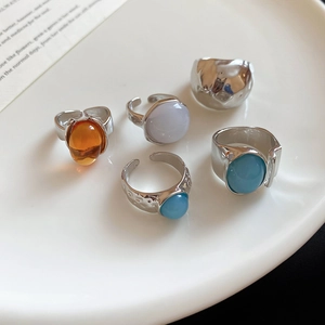Detail of silver geometric rings with amber and blue gemstones on a white ceramic plate