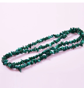 Macro shot of natural green malachite irregular crystal stone necklace on pink background