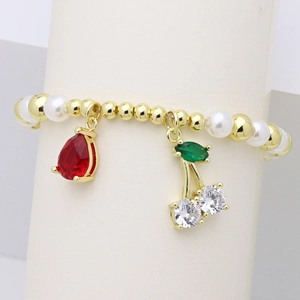 Dettaglio di bracciale con perle dorate, accenti di perla e ciondoli a forma di ciliegia