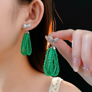 Detail of green beaded tassel earrings with silver bow design and sparkling rhinestones