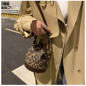 Detail of a brown leather and leopard print bucket bag held by a model in a trench coat