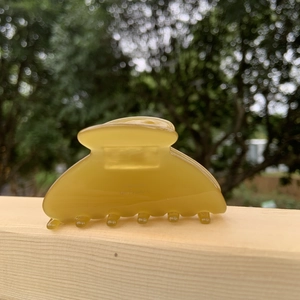 Floral yellow acetate claw clip with gold label on wooden background outdoors
