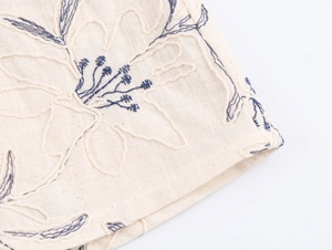 Detailed macro view of navy blue floral embroidery on beige linen fabric texture