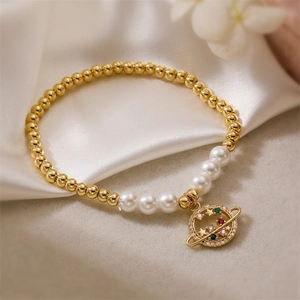 Vue rapprochée du bracelet en perles dorées avec pendentif saturne en zircon sur soie