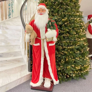 Life-size singing and dancing Santa Claus statue holding a teddy bear by a Christmas tree