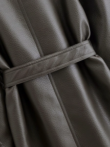 Gros plan sur la texture grainée du trench-coat en cuir vert olive foncé avec ceinture