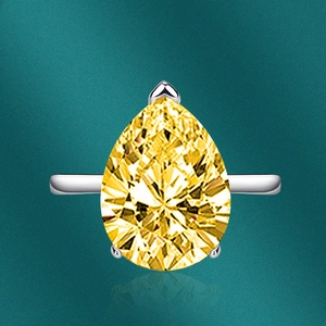 Macro view of pear-cut yellow gemstone ring with silver band on a dark green background