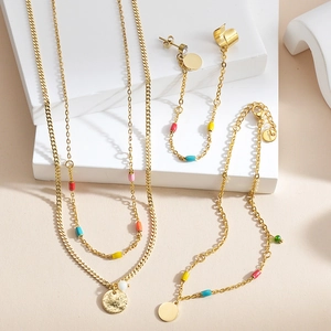 Detail of gold stainless steel jewelry set with colorful enamel beads on a clean background
