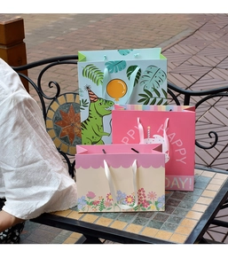 Three cute gift bags with dinosaur and cake designs on a vintage outdoor table