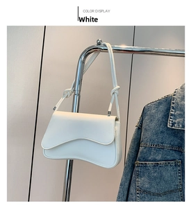 Close-up of a white leather shoulder bag with asymmetrical flap and knot detail