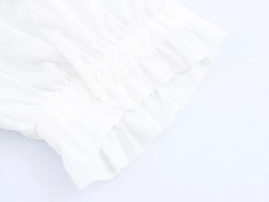 Detailansicht der weißen Puffärmelmanschette mit Rüschensaum und rundem Knopfdetail