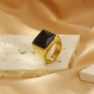 Bold gold titanium ring with a square black gemstone on a white marble background