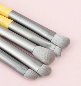 Macro view of 5-piece eye makeup brush set with yellow handles on pink background