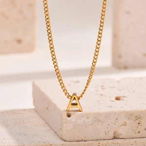 Detail view of gold letter A pendant on a stainless steel cable chain over beige stone