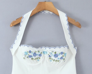 Detail of white halter neck dress with blue floral embroidery and scalloped edges