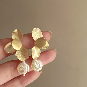 Detailed close-up of golden petal stud earrings with baroque pearl drops held by hand