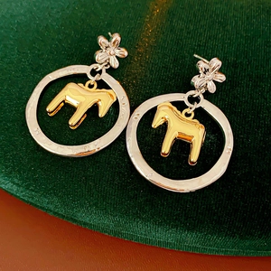 Detail of silver flower earrings with hollow round hoop and golden pony pendant