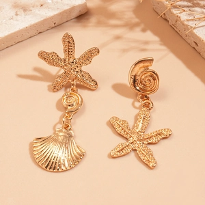 Golden asymmetrical sea shell and starfish drop earrings for women on stone background