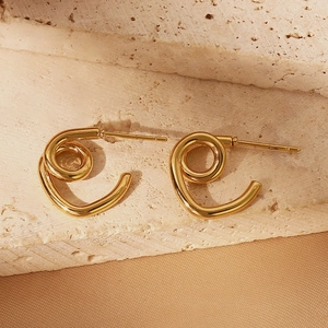 Detailed view of golden spiral geometric stud earrings on beige natural stone and silk