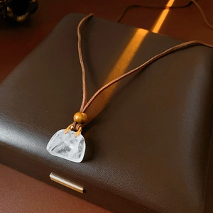 Close-up of irregular clear quartz pendant on brown leather cord over a textured box