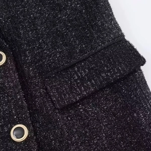 Close-up of black tweed fabric with metallic yarn and gold-rimmed decorative button
