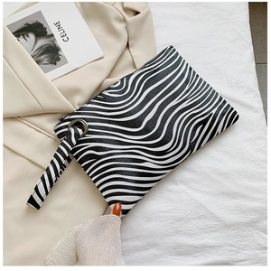 Detail of zebra pattern clutch bag with wristlet and metallic ring on beige blazer background
