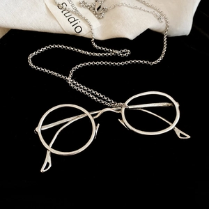Close-up of a silver-toned vintage round glasses pendant with a sleek chain on velvet