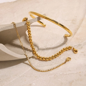 Empilement artistique de bracelets chaîne en titane doré et jonc en zircone sur pierre