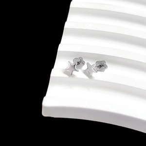 Close-up of minimalist silver star stud earrings on a white geometric display stand