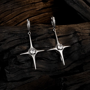 Silver four-pointed star drop earrings with clear zircon on a dark wood background