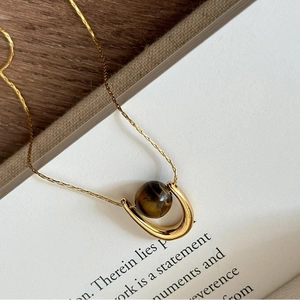 Detail of a U-shaped gold necklace featuring a brown tiger eye stone on book pages