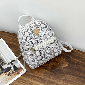 Close-up of black and white snakeskin pattern backpack with gold hardware on wood surface