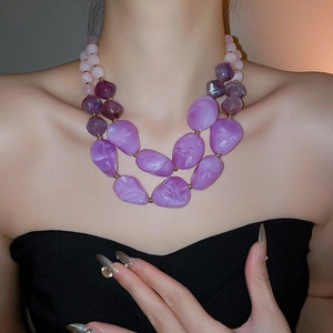 Detail of layered necklace with purple acrylic beads and golden metal spacers on a neck